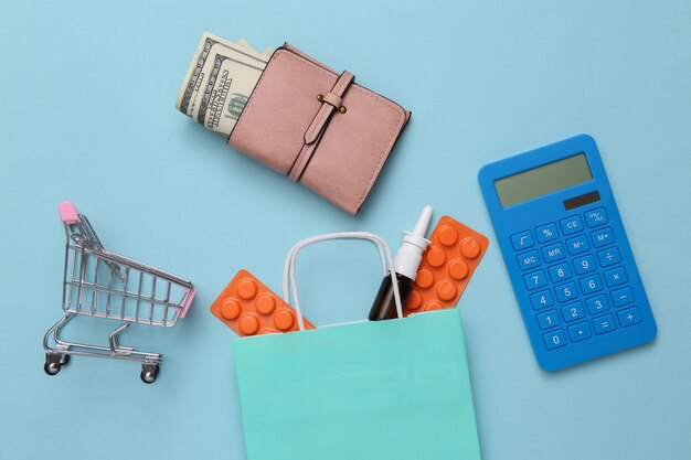 Bolsa de compras y carrito con monedero de medicamentos y calculadora sobre fondo azul Vista superior