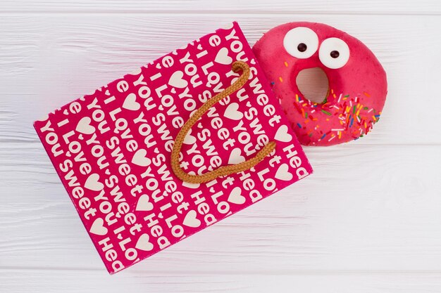 Bolsa de compras y donut sobre fondo blanco de madera. Bolsa de regalo y donut rosa divertido. Concepto de compras navideñas.