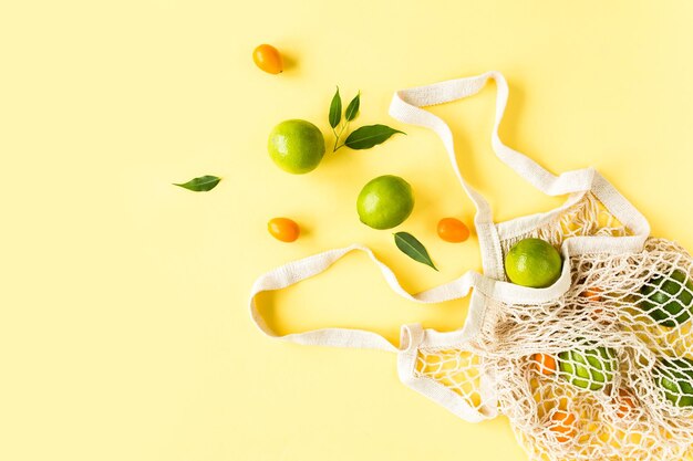 Bolsa de compras de malla con lyme sobre fondo amarillo Patrón hecho de frutas tropicales de verano Concepto de comida Vista superior plana