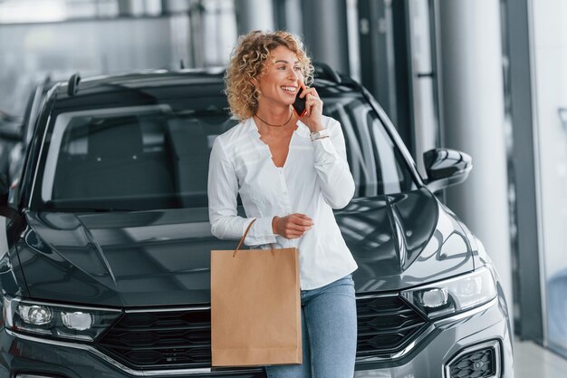 Con bolsa de compras Mujer con cabello rubio rizado está en autosalon