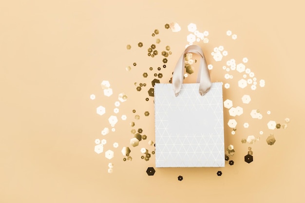 Bolsa de compras de papel y destellos hexagonales de moda sobre fondo beige concepto de venta de vacaciones en tonos monocromáticos