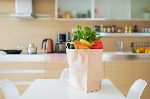 Bolsa de compras de papel llena de productos comestibles en la mesa de la cocina