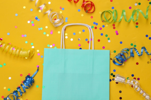 Bolsa de compras con serpentina de colores y confeti sobre fondo amarillo Día de compras