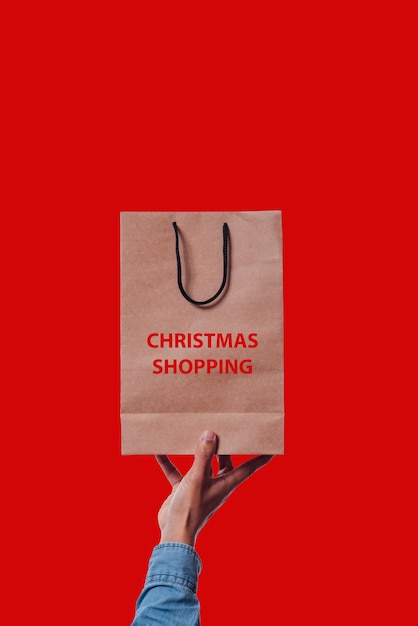 Bolsa de compras con texto de compras navideñas sobre fondo rojo.