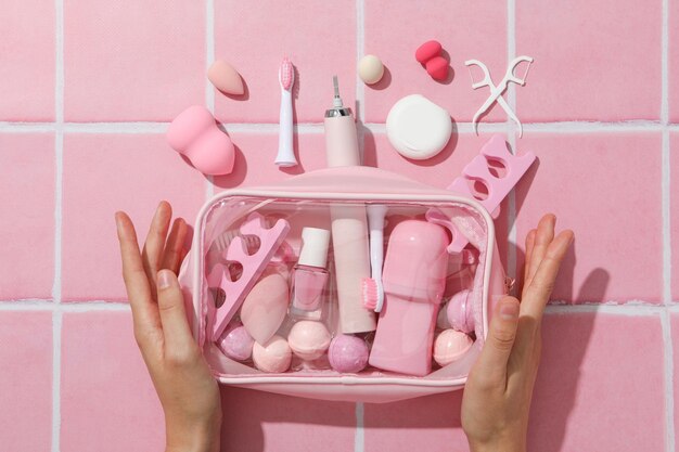 Bolsa de cosméticos con cosméticos y cepillo de dientes a mano en la vista superior de fondo rosa