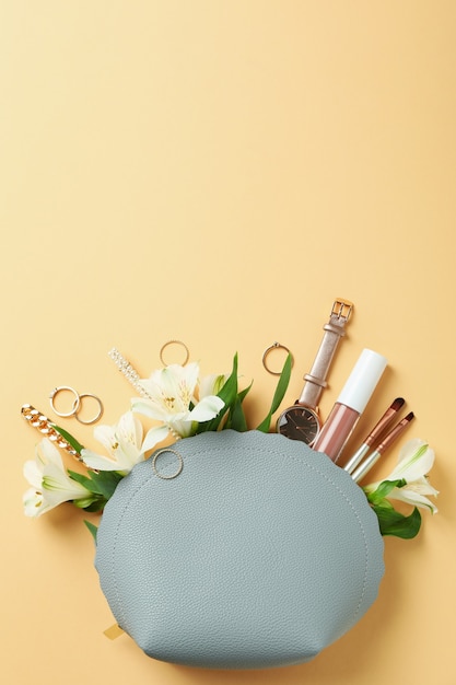 Bolsa de cosméticos con cosméticos, joyas y alstroemeria sobre fondo beige