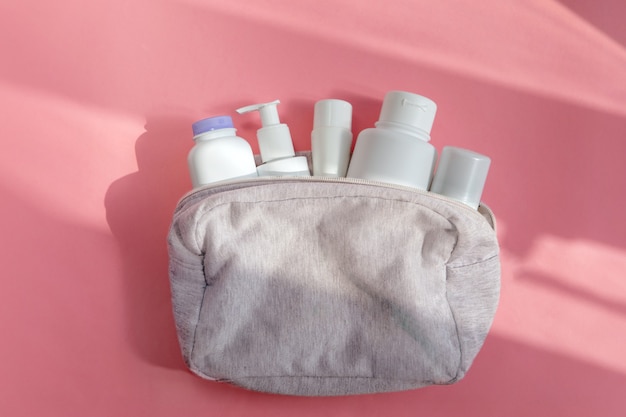 Bolsa de cosméticos con productos para el cuidado de la piel en mesa rosa