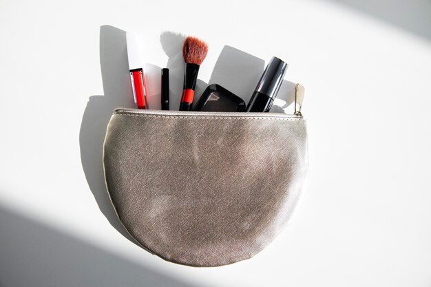 Bolsa de cosméticos con rímel y cosméticos de maquillaje en una mesa blanca al sol de la mañana Vista superior plana