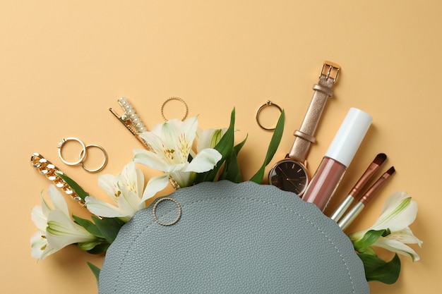 Bolsa de cosméticos com cosméticos, joias e alstroemeria em fundo bege