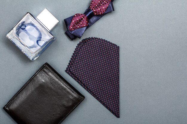 Bolsa de couro, colônia para homem, gravata borboleta e lenço em fundo cinza. Acessórios para homem. Vista superior com espaço de cópia
