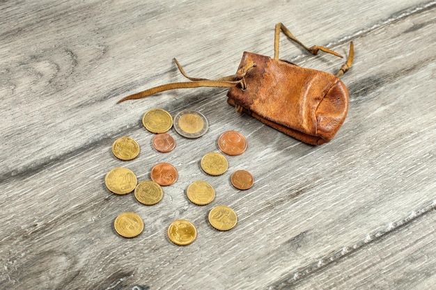 Bolsa de moedas de couro marrom desgastada velha, com moedas de euro derramadas na mesa de madeira cinza.