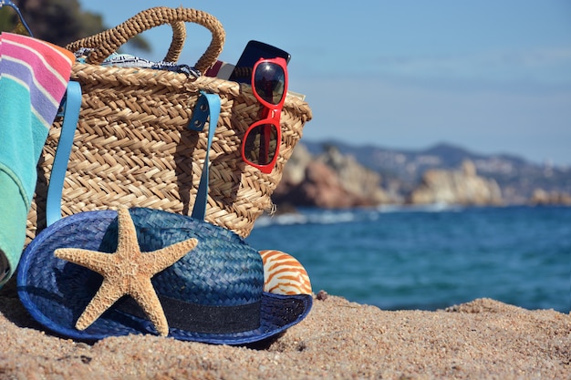 Bolsa de praia com um livro e um telefone e óculos de sol, acompanhados por uma estrela do mar