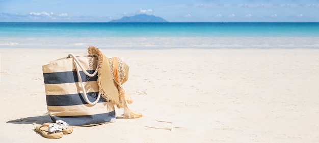 Bolsa de praia listrada, chapéu de palha e chinelos em uma praia tropical