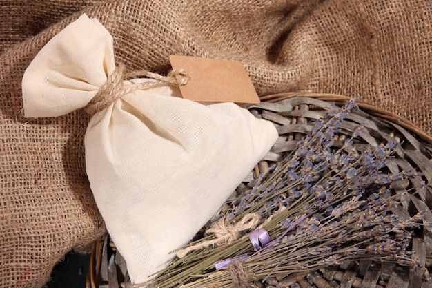 Foto bolsa de sachê têxtil com flores secas de lavanda em mesa de madeira sobre fundo de saco