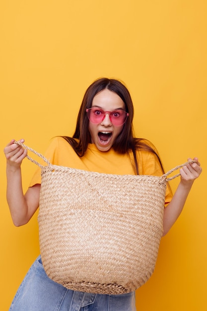 Bolsa de vime jovem e bonita na mão óculos rosa fundo amarelo