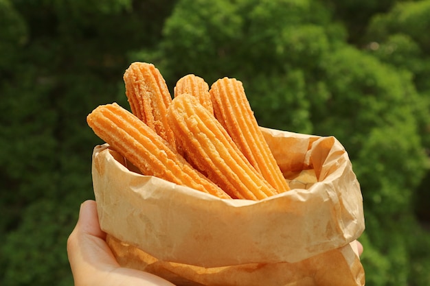 Una bolsa de deliciosos palos de churros en la mano con un follaje verde borroso en el fondo