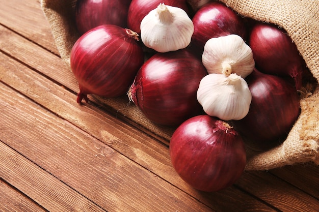 Bolsa esparcida con cebolla roja y ajo sobre fondo de madera