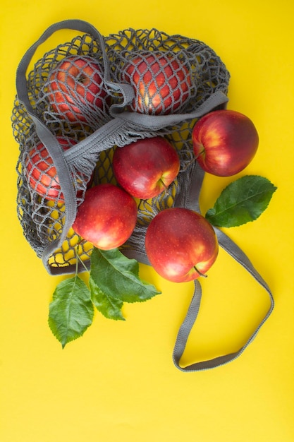 Bolsa gris de compras de malla con manzanas rojas sobre fondo amarillo Sin concepto de bolsa de plástico Vista superior Ubicación vertical