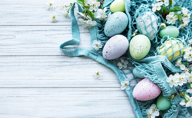 Bolsa de hilo con huevos de Pascua y flor de primavera en la esquina de una mesa de madera rústica