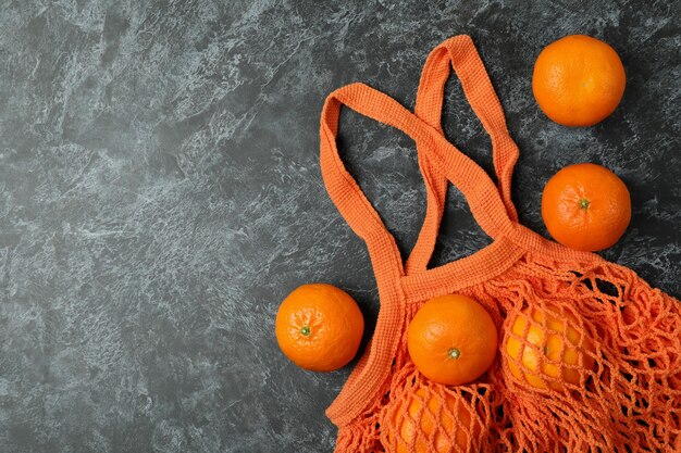 Bolsa de hilo con mandarinas sobre fondo negro ahumado