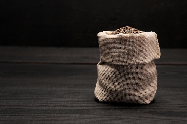 Bolsa llena de semillas de chía naturales orgánicas sobre fondo o mesa de madera oscura.