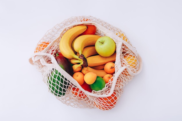 Bolsa de malla de algodón con frutas frescas de colores sobre fondo claro, vista superior. Concepto de desperdicio cero