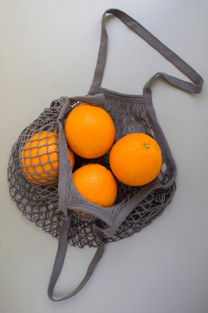 Bolsa de malla de compras gris con naranjas sobre fondo gris. Sin concepto de bolsa de plástico. Vista superior. Ubicación vertical.