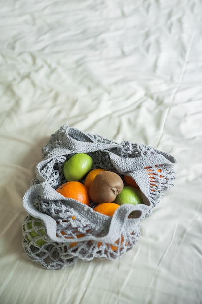 Bolsa de malla gris con espacio de primer plano y copia de naranjas amarillas. Bolsa ecológica artesanal sobre textiles