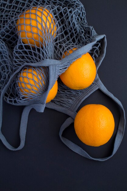 Bolsa de malla gris con naranjas sobre fondo negro sin concepto de bolsa de plástico. Vista superior. Ubicación vertical.