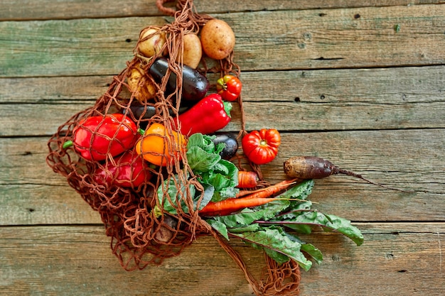 Bolsa de malla reutilizable para compras de cadena ecológica plana con surtido de verduras frescas, alimentos bio saludables y orgánicos sobre fondo de madera, estilo de mercado rural, abarrotes, comida vegetariana dietética.