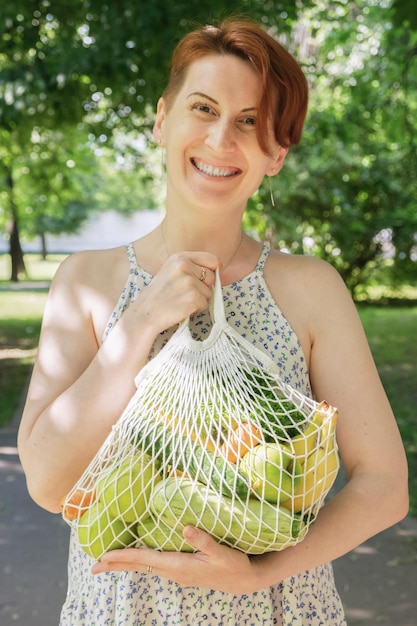 Bolsa de malla tejida con verduras y frutas en manos de una mujer
