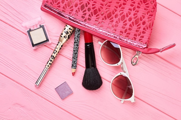 Bolsa de maquillaje con cosméticos y accesorios. Kit de cosméticos de maquillaje, neceser y artículos esenciales de moda de belleza. Esenciales de belleza femenina sobre fondo de madera rosa.