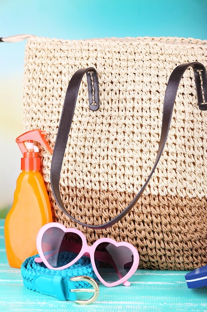 Bolsa de mimbre de verano con accesorios sobre fondo de naturaleza.