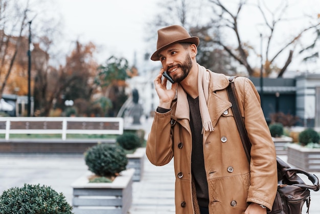 Con bolsa Modelo masculino joven en ropa de moda está al aire libre en la ciudad durante el día