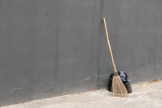 Una bolsa negra de basura y escoba vieja contra una pared gris., Con espacio de copia para el texto.