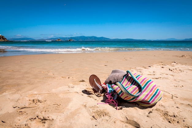 Bolsa, óculos escuros, chinelos e toalha na praia