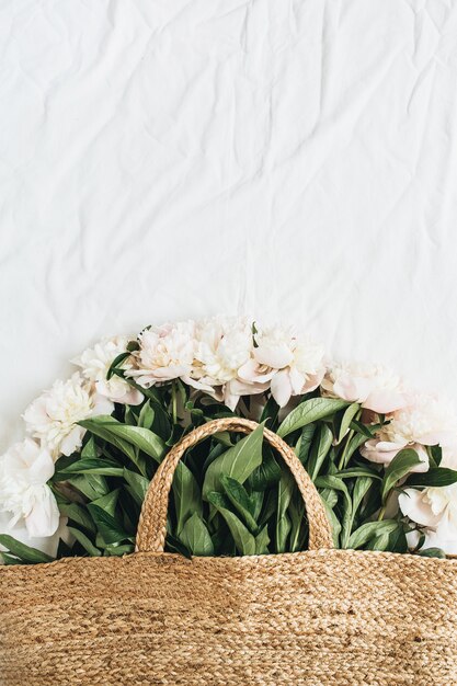 Bolsa de paja con flores de peonía blanca sobre superficie blanca