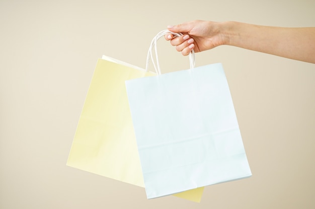 Bolsa de papel amarillo y azul, embalaje ecológico en una mano femenina sobre un fondo beige, espacio para texto.