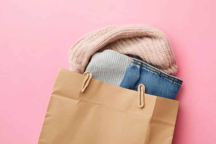 Bolsa de papel artesanal con ropa en fondo rosa para la venta