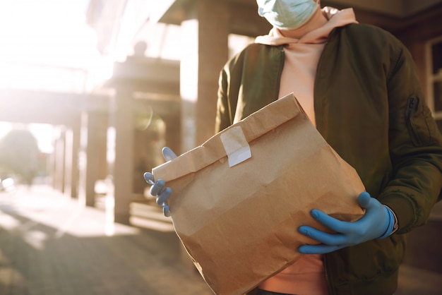La bolsa de papel con comida y café en manos del servicio de mensajería en la ciudad de cuarentena. Servicio de entrega bajo cuarentena, brote de enfermedad, condiciones de pandemia de coronavirus covid-19.