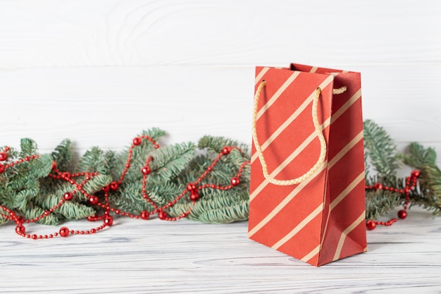 Bolsa de papel de compras navideñas con ramas de abeto decoradas con cuentas rojas