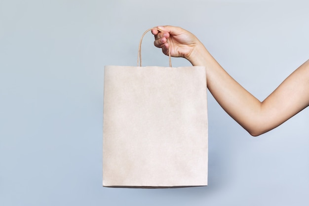 Bolsa de papel ecológico con copia espacio vacío para el logotipo en una mano femenina sobre un fondo gris