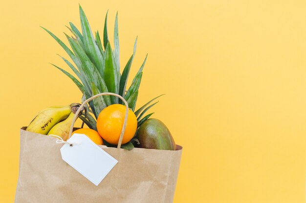 Bolsa de papel y etiqueta de cartón sin rotulación con fruta variada sobre fondo amarillo. Bosquejo.