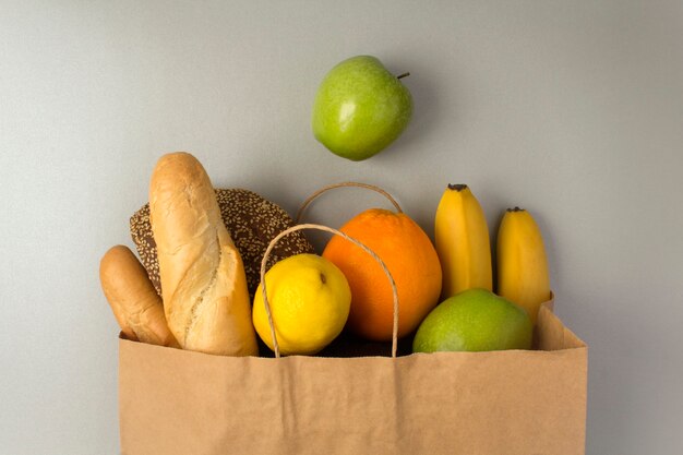 Bolsa de papel con frutas y pan sobre la superficie gris