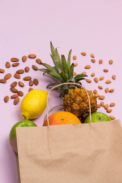 Bolsa de papel con frutas sobre fondo rosa, manzana, limón, pomelo, piña y nueces