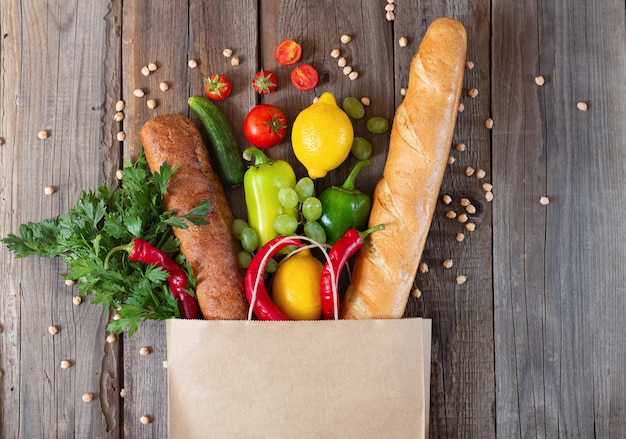 Bolsa de papel llena de diferentes alimentos en la mesa de madera