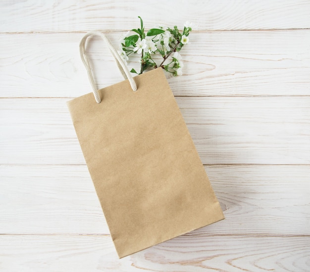 Bolsa de papel marrón con asas y flores en el interior sobre fondo blanco de madera