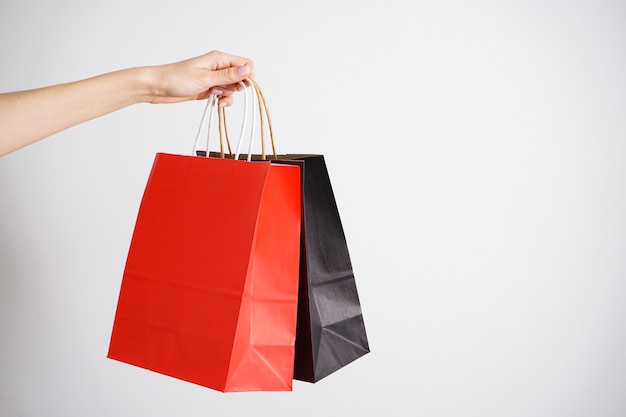 Bolsa de papel negro y rojo, embalaje ecológico en una mano femenina sobre un fondo blanco, espacio para texto.