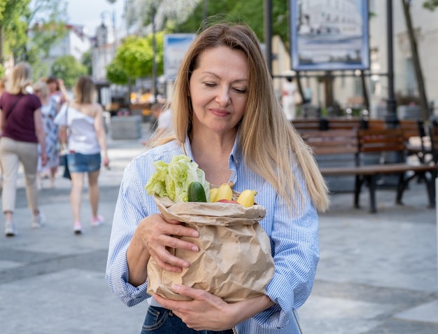 Una bolsa de papel de primer plano con verduras y frutas en manos femeninas