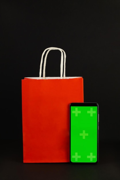 Bolsa de papel roja y teléfono de pantalla verde sobre fondo negro. Black Friday El concepto de venta, promoción